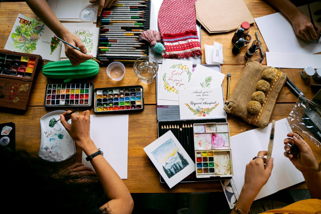 Top view of artists working with watercolor paints and art supplies in a creative workshop setting.