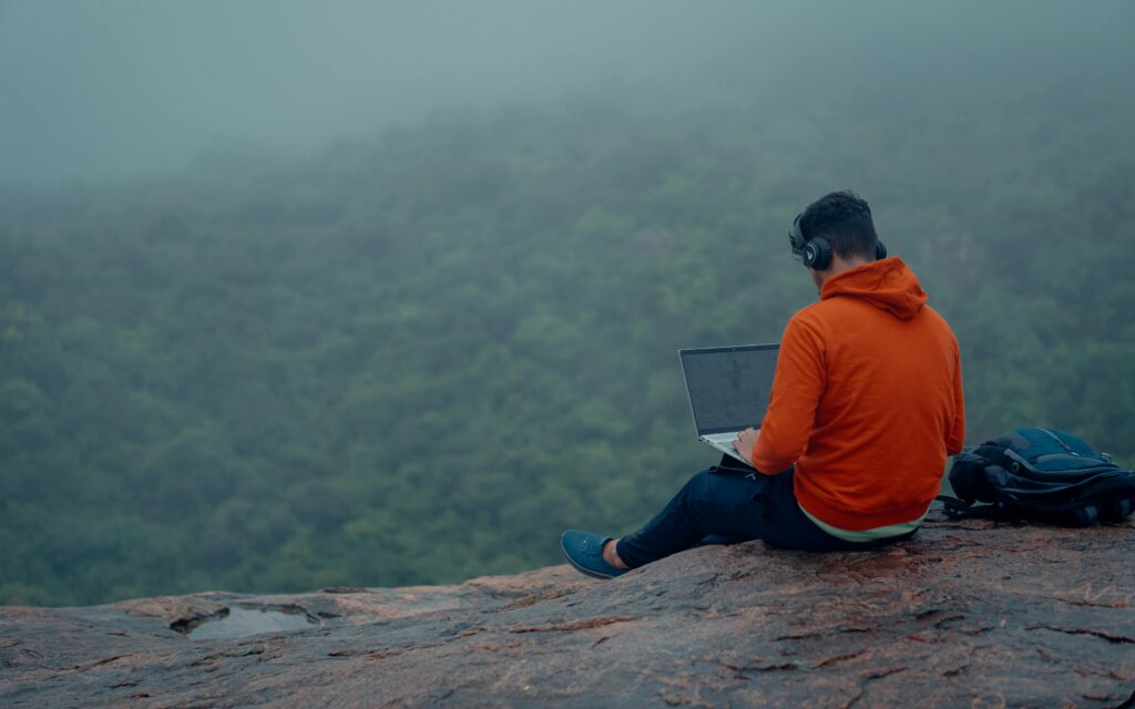 Man in hoodie working on laptop in misty forest, Bengaluru. Modern remote work.